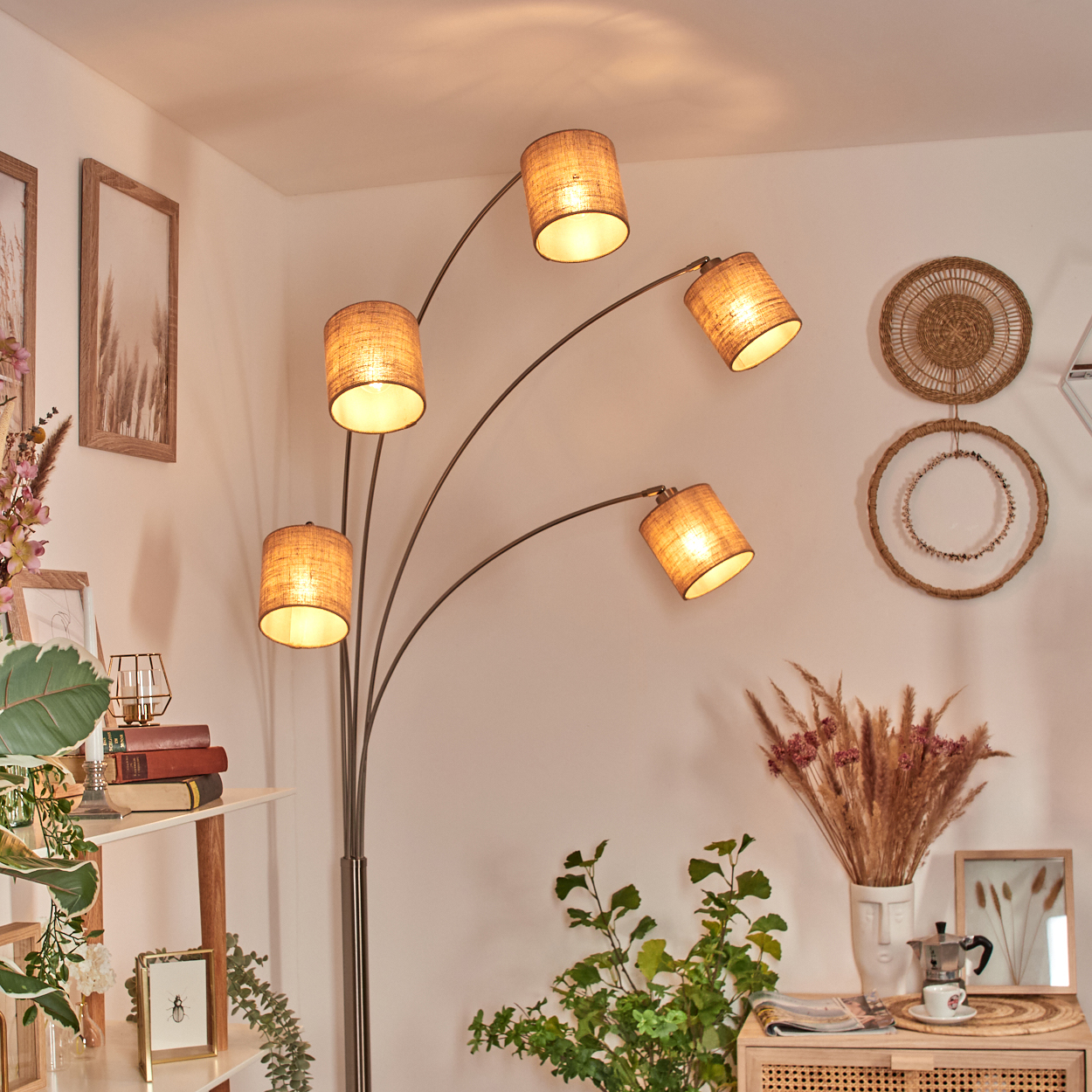 Eine moderne Stehlampe mit fünf Lampenschirmen. Der Raum hat Dekor und Pflanzen. Auf einem Holzschrank steht ein Kaffeeset.