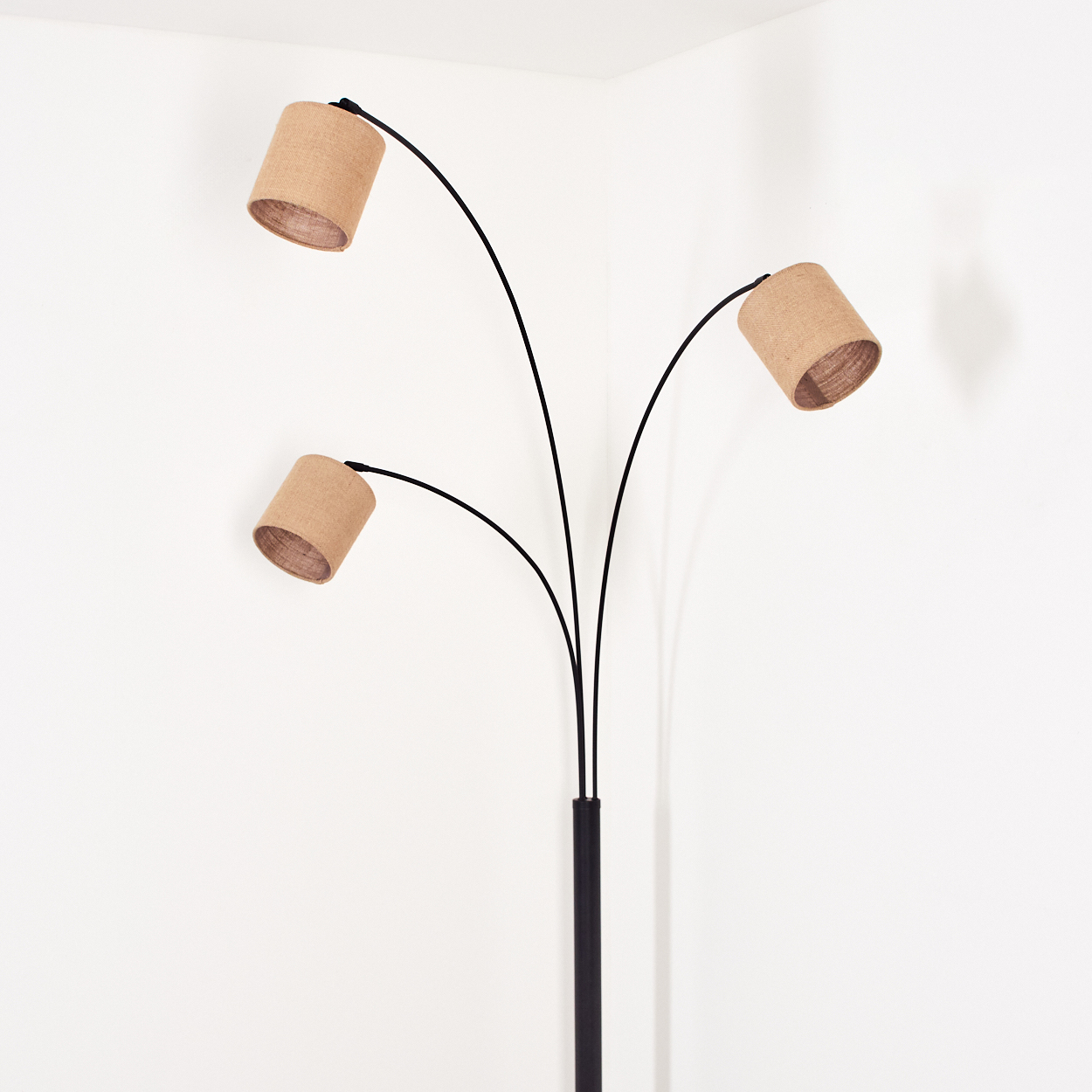 Eine Stehlampe mit drei Lampenschirmen. Die Lampenschirme sind beige, der Ständer ist schwarz und der Hintergrund ist eine weiße Ecke.
