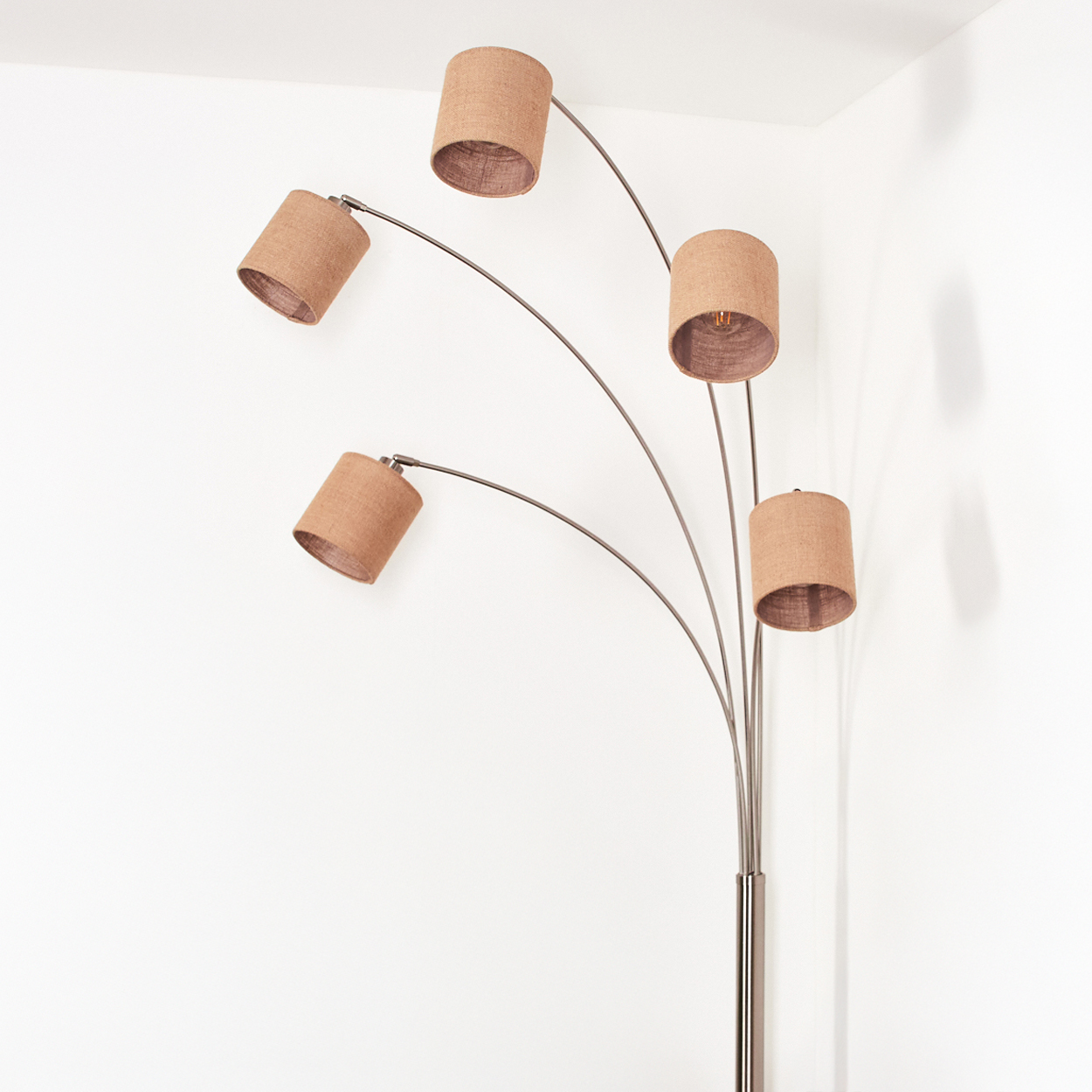 Eine Stehlampe mit fünf Lampenschirmen. Die Lampenschirme sind beige und das Gestell ist metallisch. Die Lampe steht in einer weißen Ecke.
