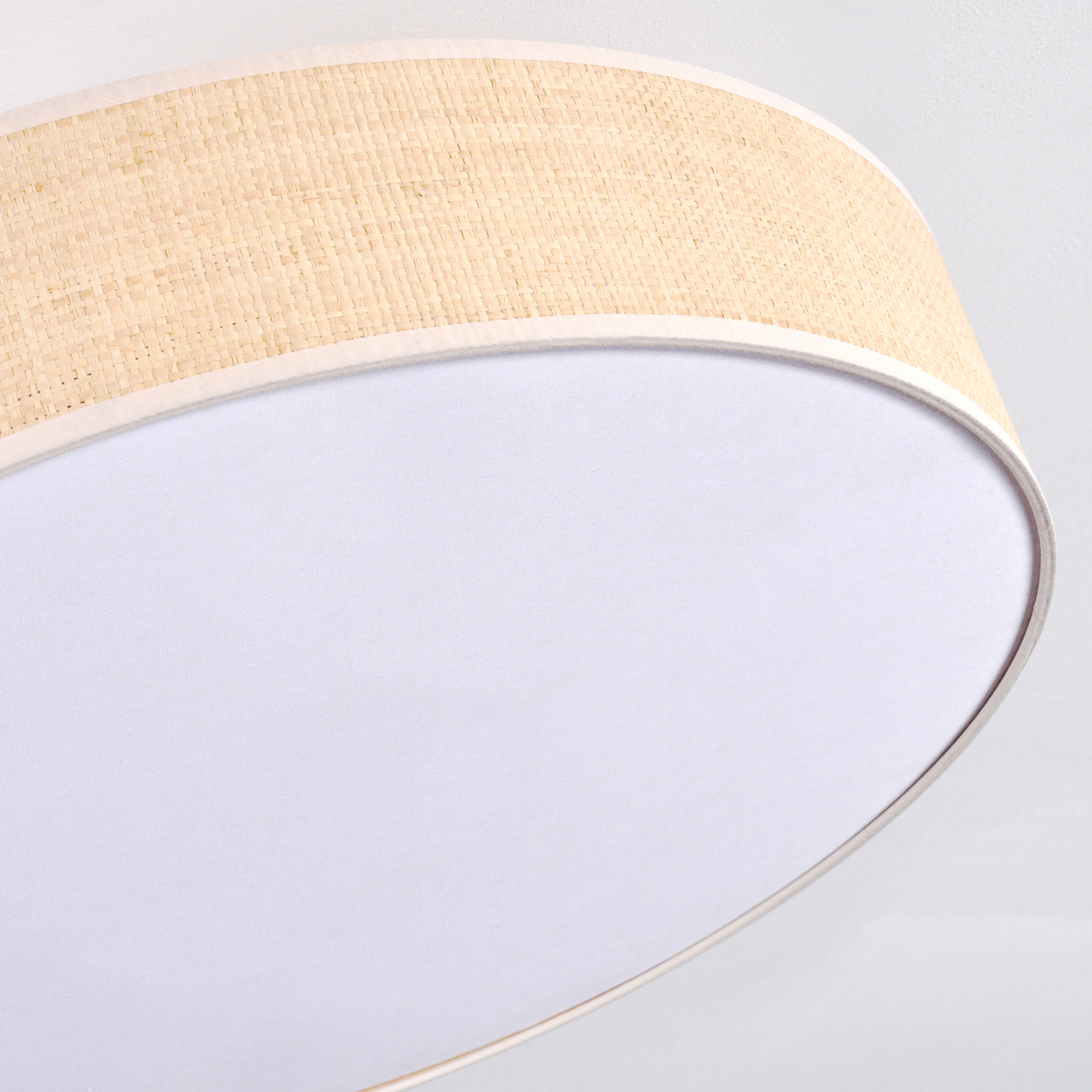 Nahaufnahme einer Lampe. Beiger gewebter Schirm umgibt einen weißen Diffusor. Der Hintergrund ist eine weiße Oberfläche.
