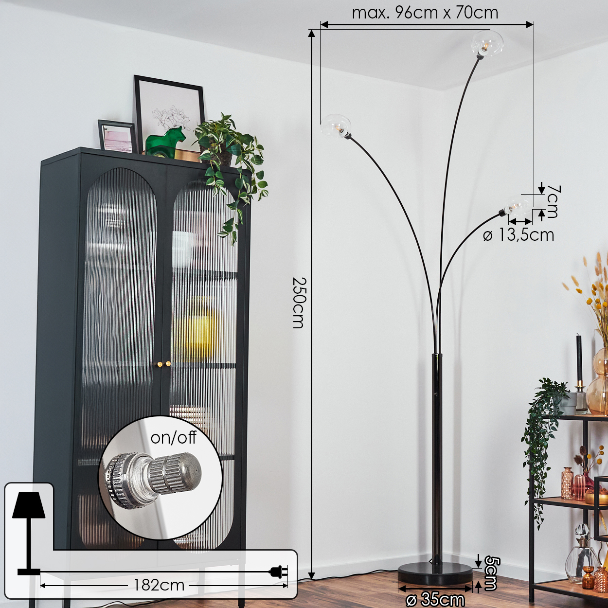 Eine moderne Stehlampe mit drei Glaskugeln. Neben der Lampe steht ein dunkler Schrank mit Pflanzen.