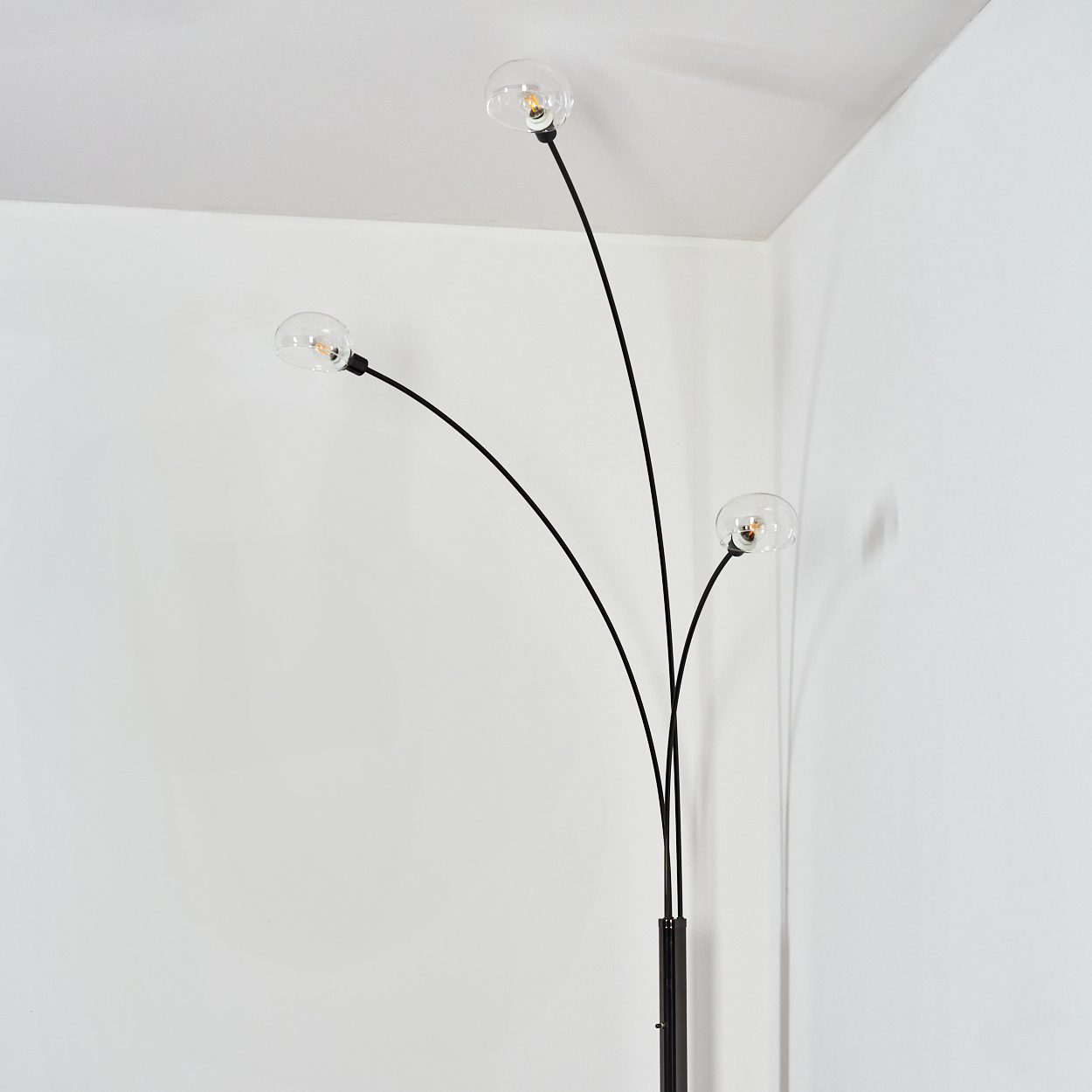Eine moderne schwarze Stehlampe mit drei gebogenen Armen, die jeweils eine klare, runde Glühbirne halten. Sie steht vor weißen Wänden.