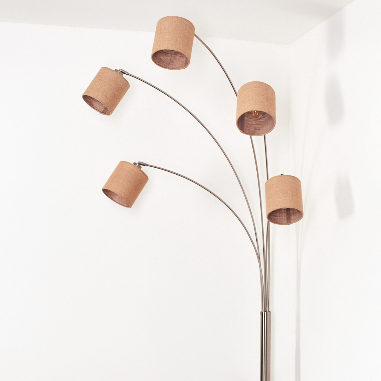 Eine moderne Stehlampe mit fünf Lampenschirmen. Die Schirme sind beige, das Gestell silbern. Sie steht in einer weißen Ecke.