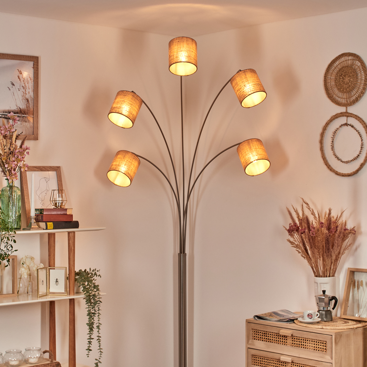Eine Stehlampe mit 5 Lampenschirmen. Daneben ein Regal mit Büchern und Dekorationen. Rechts ein Holzschrank mit Kaffeeservice.