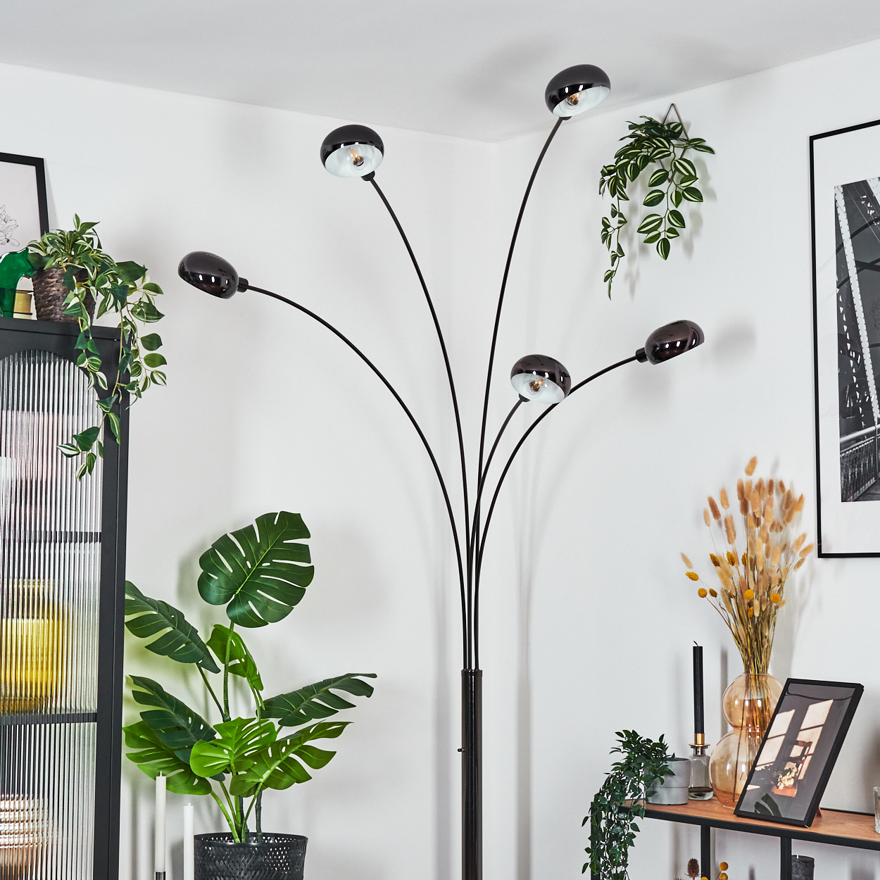 Eine moderne schwarze Stehlampe mit fünf Lichtern. Pflanzen, Bilder und andere Dekorationen befinden sich in einem Raum darum herum.