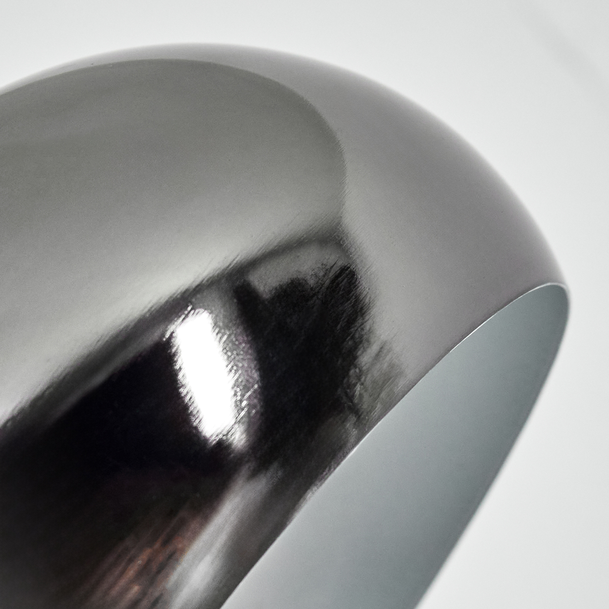Nahaufnahme eines metallischen, grauen, schalenförmigen Objekts mit reflektierender Oberfläche. Das Innere ist hellgrau. Der Hintergrund ist weiß.