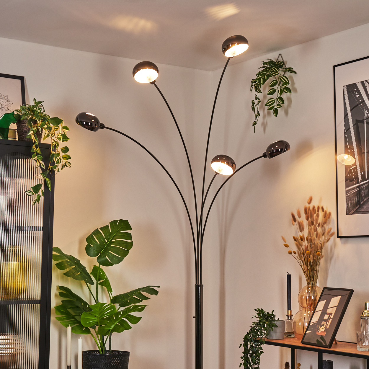 Ein modernes Wohnzimmer mit schwarzer Stehlampe, Topfpflanzen und einem gerahmten Bild. Die Lampe hat fünf Lichter.