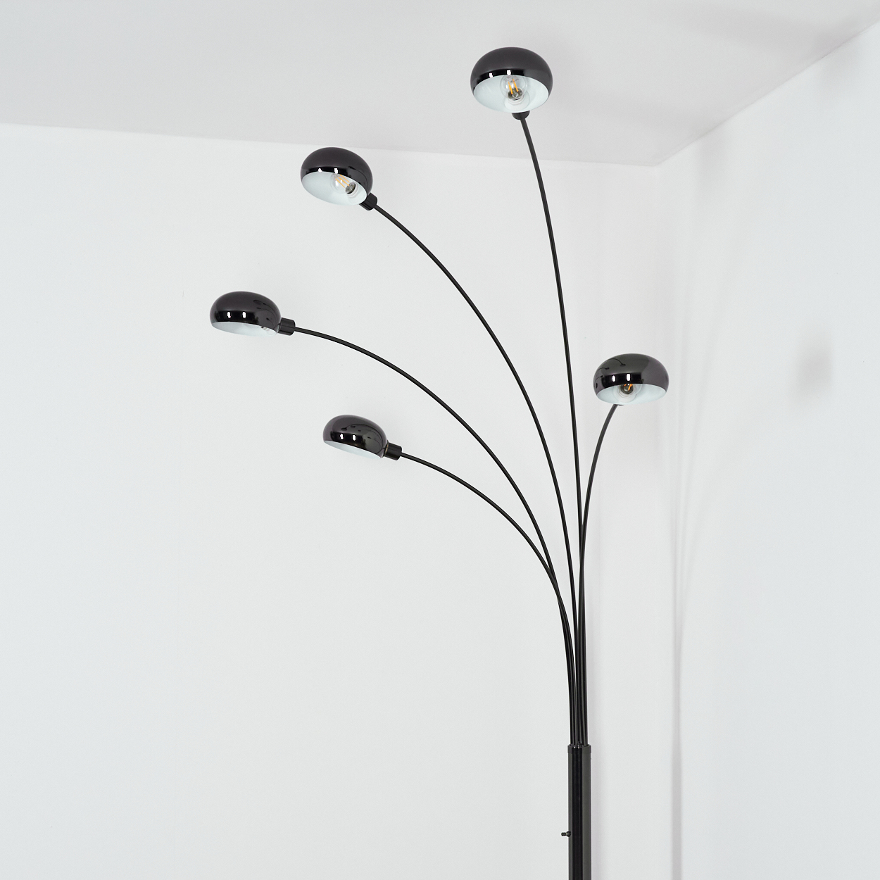 Eine moderne schwarze Stehlampe mit fünf kugelförmigen Lampenschirmen, jeweils mit einer Glühbirne. Die Lampe steht vor einer weißen Wand in einer Ecke.