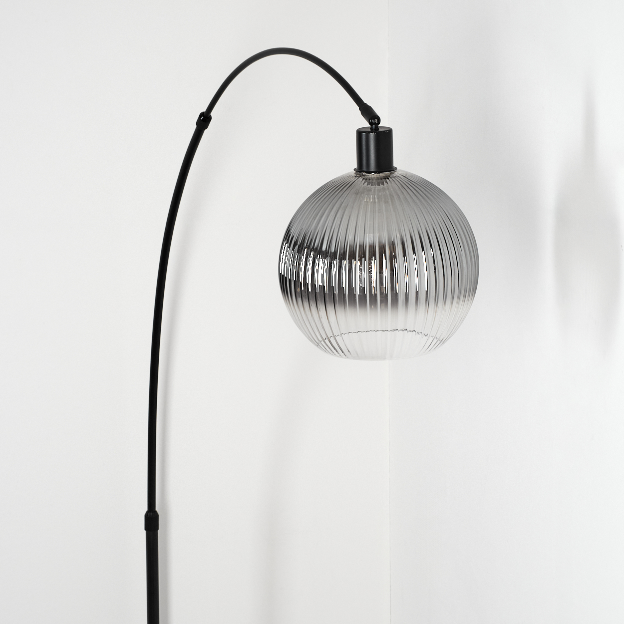 Eine moderne schwarze Lampe mit gebogenem Arm und geripptem Glaskugel. Der Hintergrund ist eine weiße Ecke.