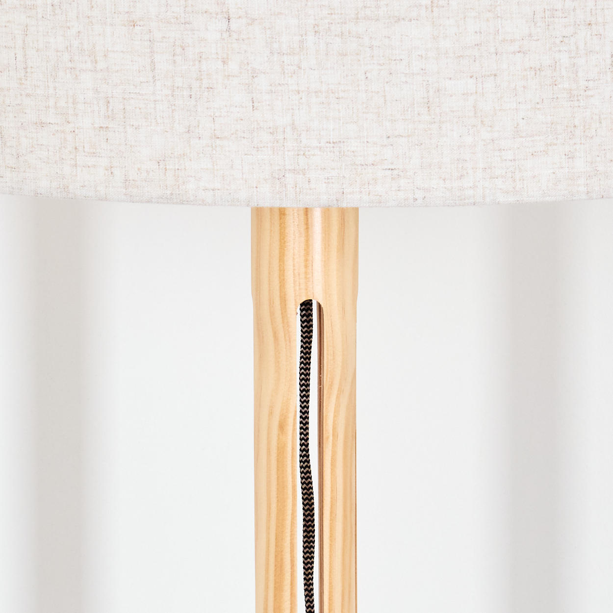 Nahaufnahme eines Lampenfußes aus Holz mit beigem Lampenschirm. Ein schwarzes Kabel verläuft durch die Mitte des Ständers.