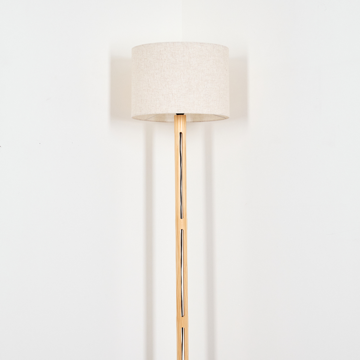 Ein beigefarbener Lampenschirm sitzt auf einer Holzlampe. Die Lampe steht vor einer weißen Wand, ihr Kabel ist sichtbar.
