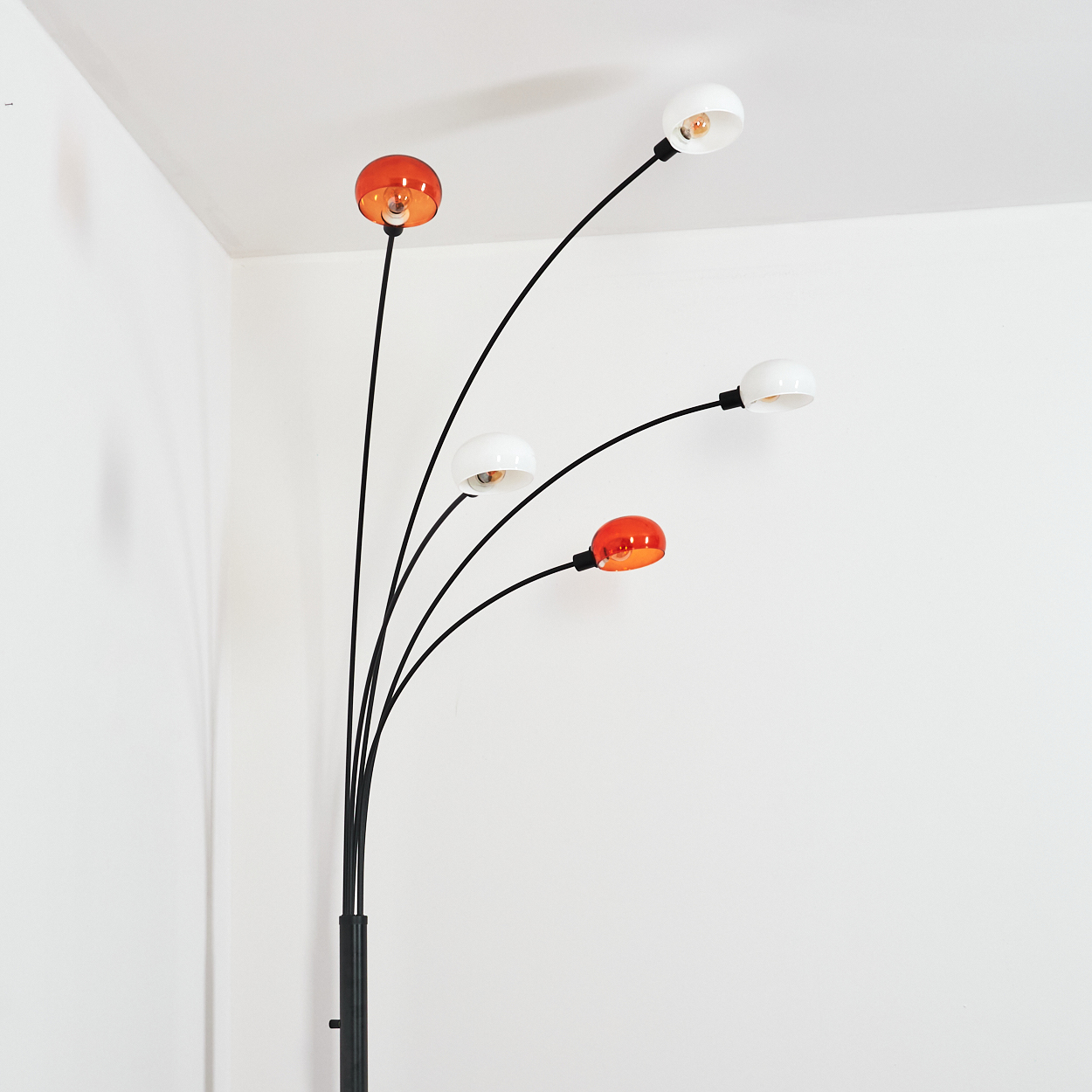 Eine moderne Stehlampe mit fünf gebogenen schwarzen Armen, die orangefarbene und weiße kugelförmige Lichter halten, vor einer weißen Wand.