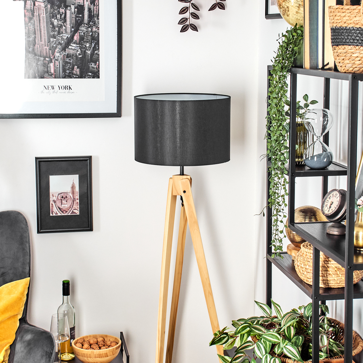 Ein Zimmer mit einer Holzlampe, einem schwarzen Schirm und einem Bücherregal mit Dekoration. An der Wand befinden sich ein New York-Bild und ein kleiner Rahmen.