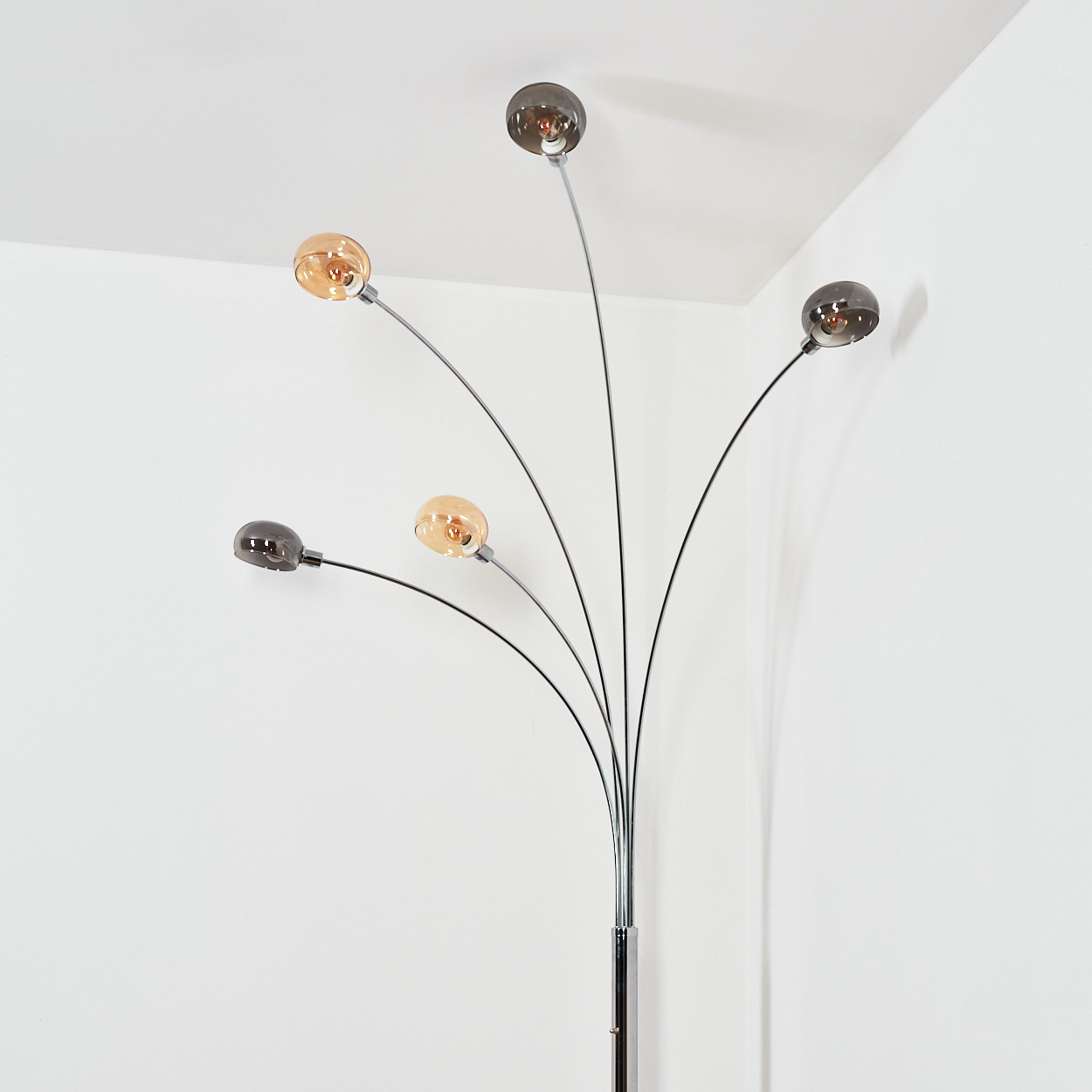 Eine moderne Stehlampe mit fünf gebogenen Armen, die jeweils ein kugelförmiges Licht halten. Einige Lichter sind bernsteinfarben, andere rauchfarben, vor einer weißen Wand.