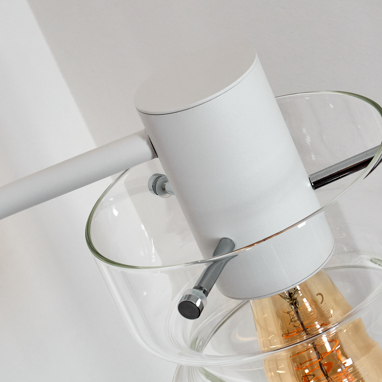 Eine moderne Lampe mit weißem zylindrischen Schirm, Glasschirm und sichtbarer Glühbirne vor weißem Hintergrund.