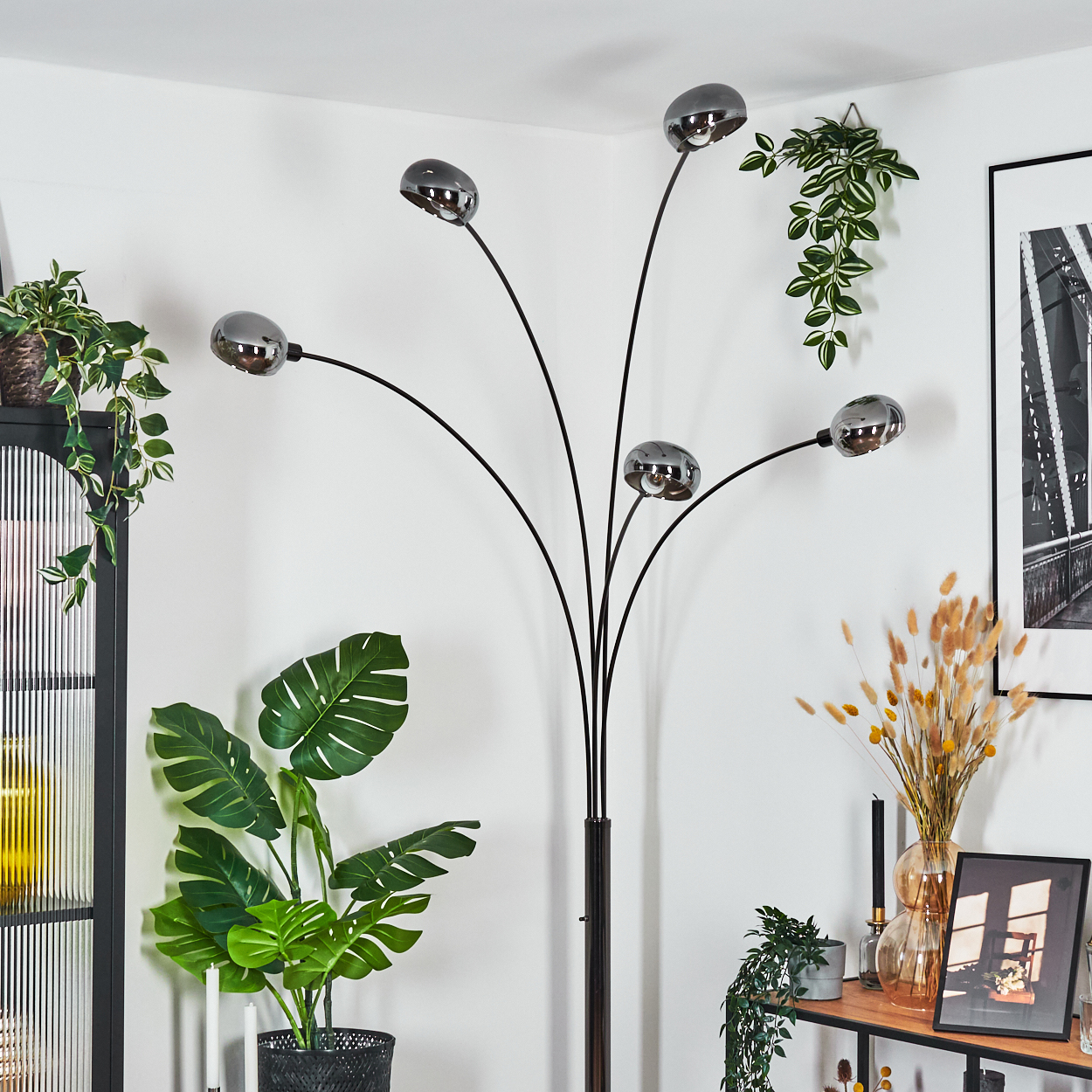 Ein modernes Wohnzimmer mit einer schwarzen Stehlampe mit fünf Lichtern, Pflanzen und einem schwarz-weißen gerahmten Bild.