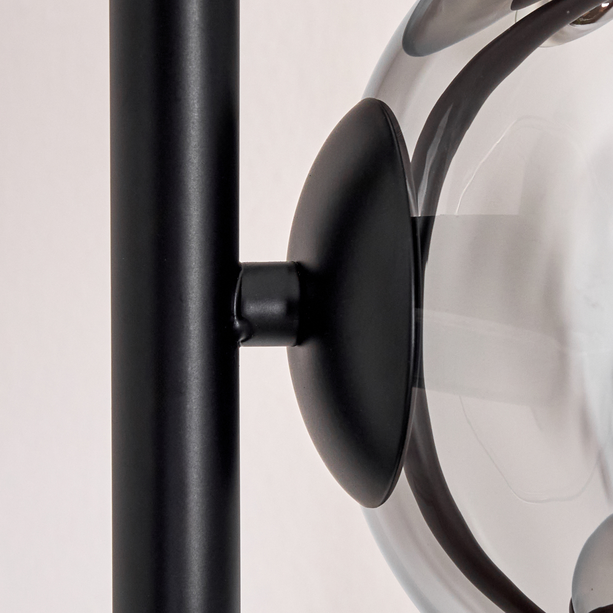 Nahaufnahme einer schwarzen Lampe. Eine schwarze Metallstange verbindet sich mit einem runden schwarzen Element, das eine klare Glaskugel hält.