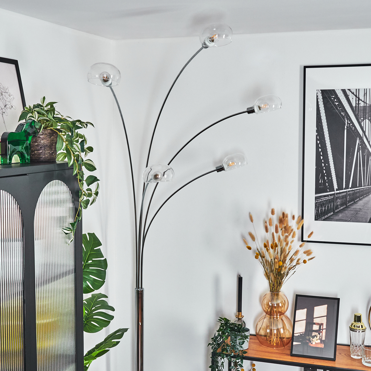 Ein modernes Wohnzimmer mit Stehlampe. Es gibt einen Schrank, Bilder, Pflanzen und eine Vase mit Blumen.
