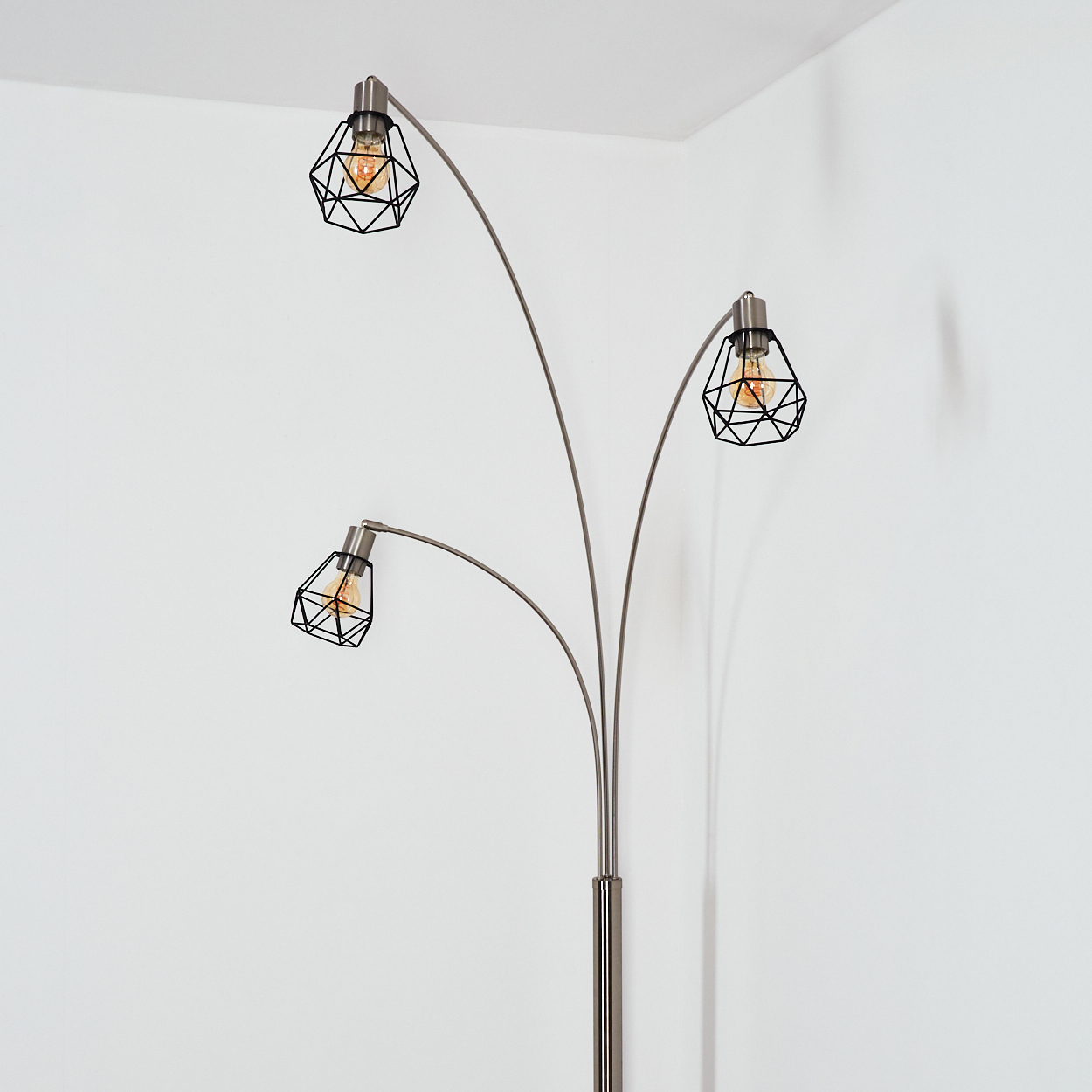 Eine moderne Stehlampe mit drei Lichtern. Jedes Licht hat einen schwarzen, geometrischen Schirm und eine warme Glühbirne. Der Ständer ist silberfarben.