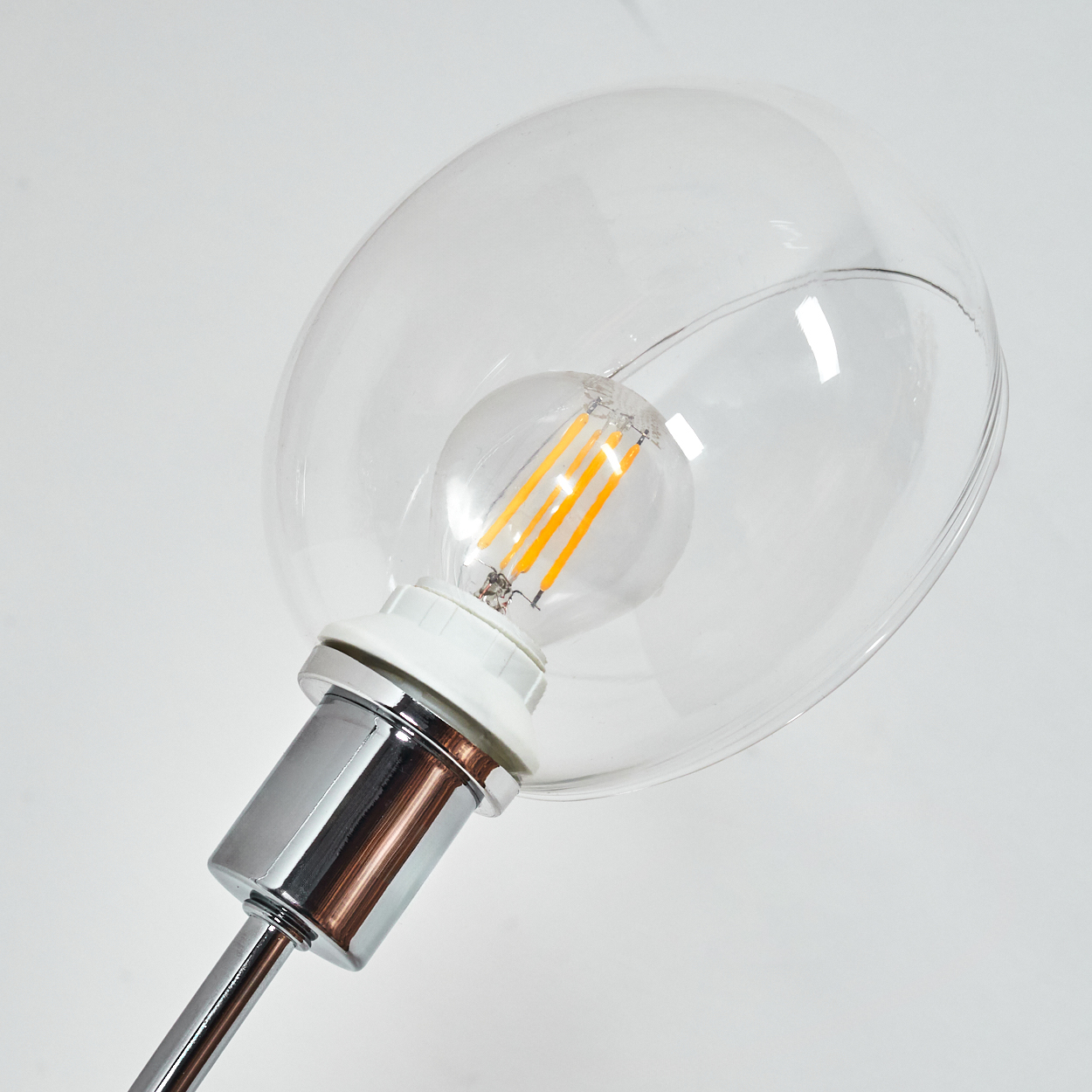 Nahaufnahme einer modernen Lampe. Sie hat eine transparente Glühbirnenabdeckung, eine Glühbirne im Inneren und einen Chrom- und Kupferstiel. Der Hintergrund ist weiß.