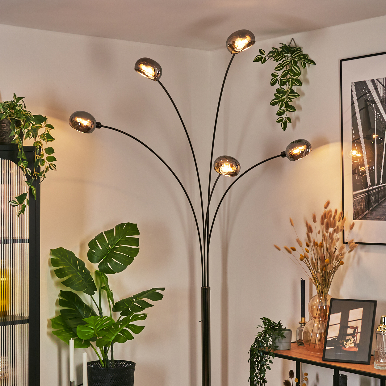 Ein modernes Wohnzimmer mit schwarzer Stehlampe, Pflanzen und einem gerahmten Brückenbild.