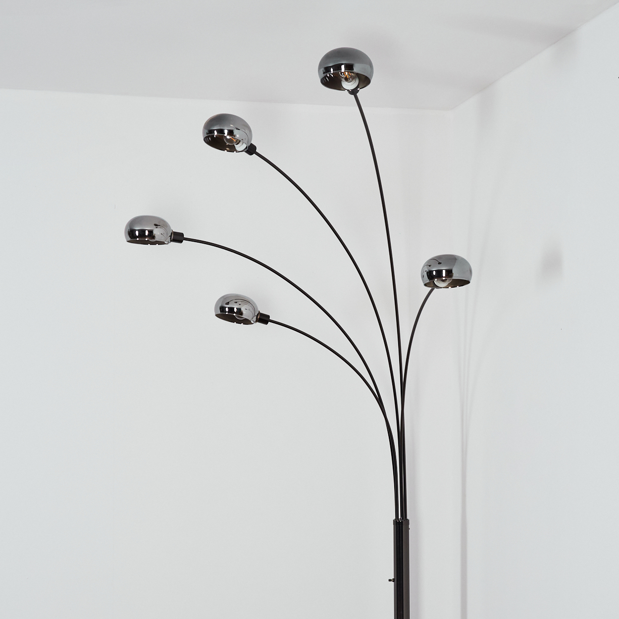 Eine moderne Stehlampe mit fünf verchromten Kugelleuchten auf schwarzen Stielen. Der Hintergrund sind weiße Wände.