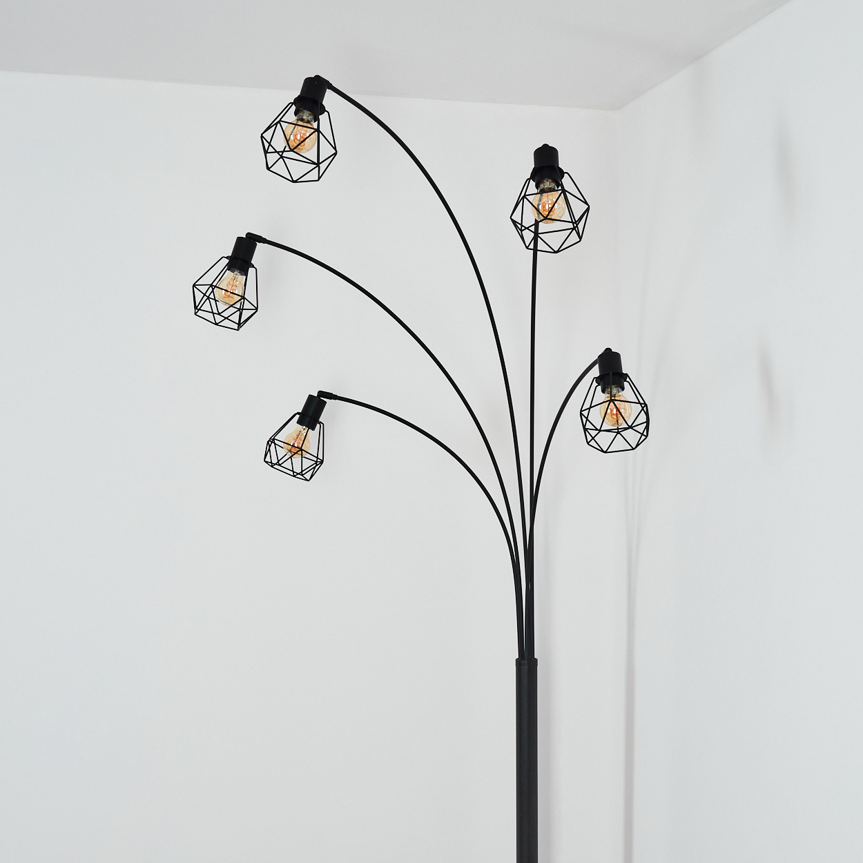 Eine schwarze Stehlampe mit fünf Lichtern, jedes in einem geometrischen Käfig, vor einer weißen Wand.