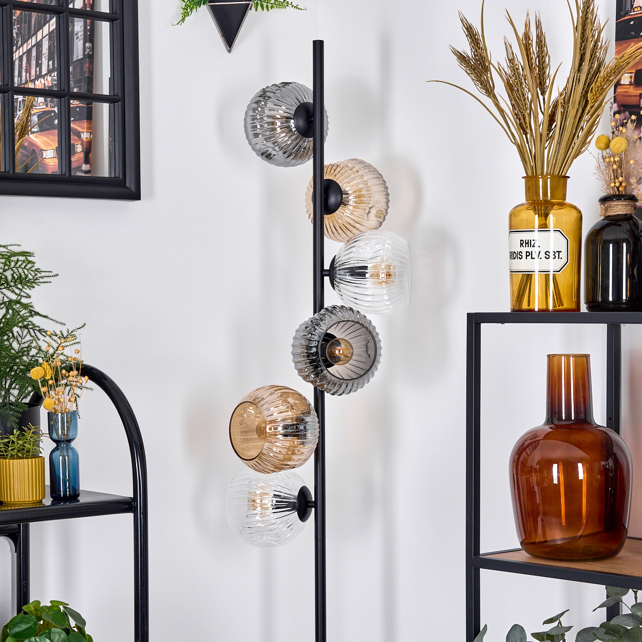 Eine moderne Stehlampe mit Glaskugelschirmen steht neben Regalen mit Vasen und Dekorationsartikeln. Ein gerahmtes Bild hängt an der Wand.