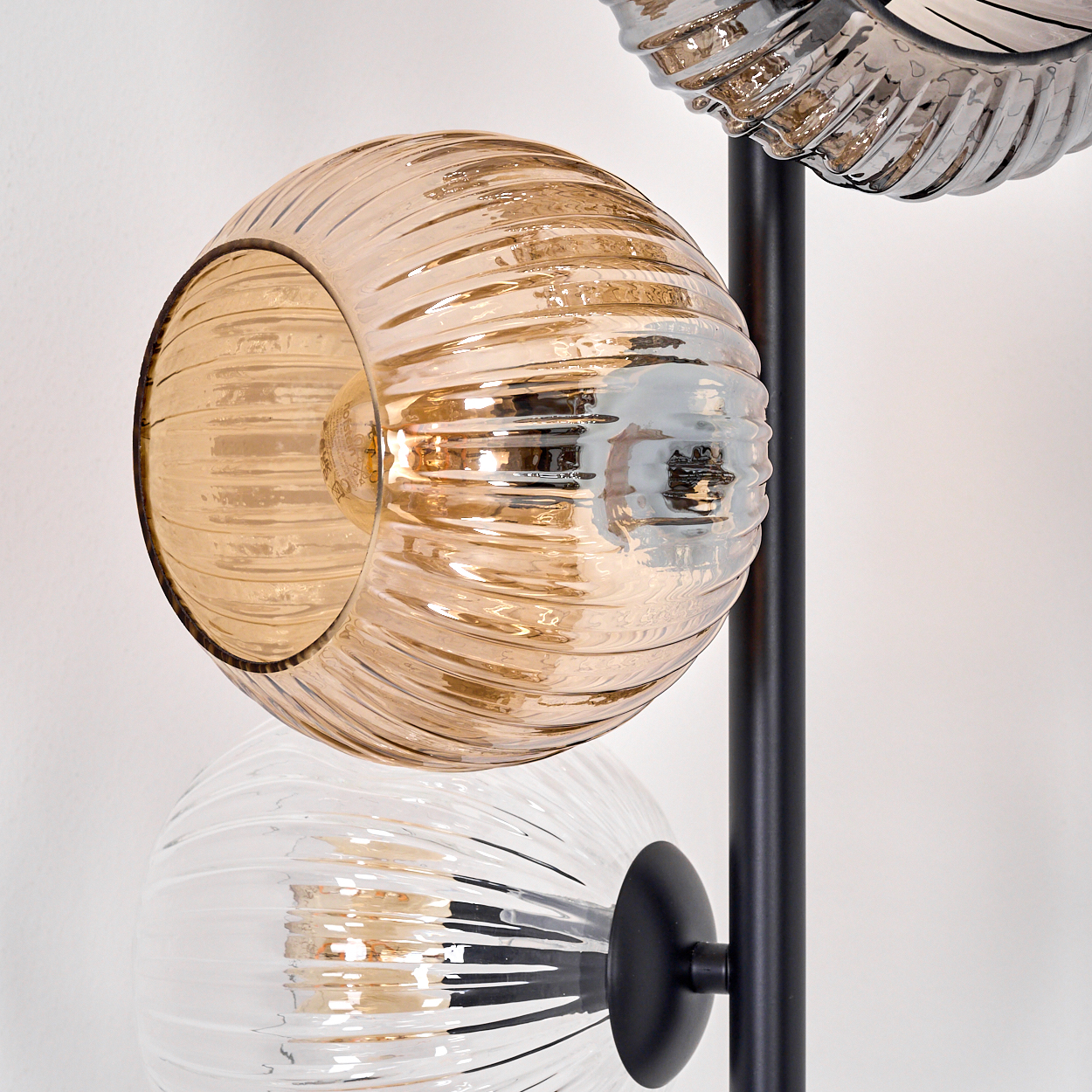 Moderne Lampe mit drei Glaskugeln. Die obere Kugel ist bernsteinfarben, die mittlere klar, und sie sind an einer schwarzen Metallsäule befestigt.