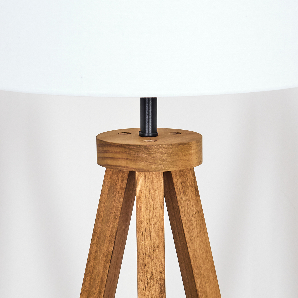 Holz-Dreibein-Lampe mit weißem Lampenschirm. Die Lampe hat einen Holzfuß und eine schwarze Metallstange.
