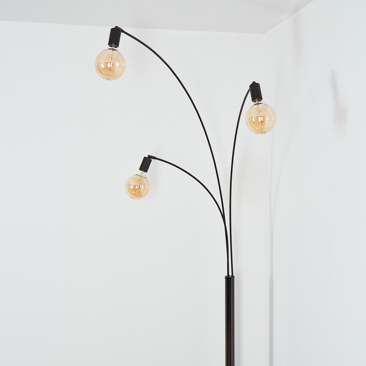 Eine moderne schwarze Stehlampe mit drei Glühbirnen in kugelförmigem Glas. Der Hintergrund ist eine weiße Wand.