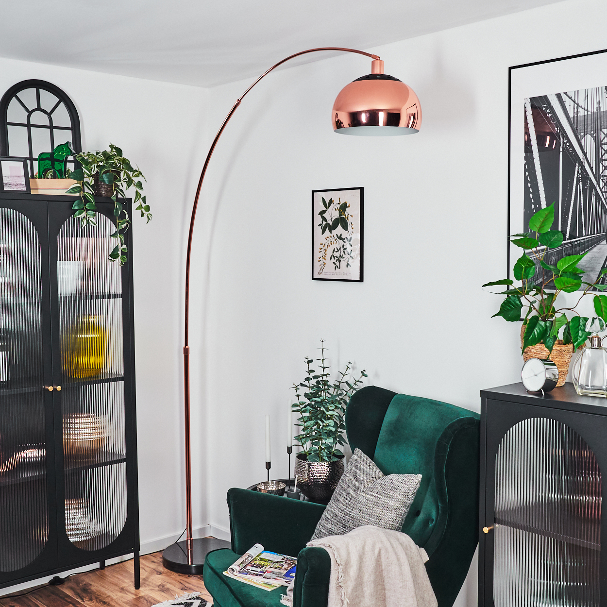 Wohnzimmer mit grünem Sessel, Kupferlampe, schwarzen Schränken, Pflanzen und einem gerahmten Brückenfoto. Gemütliche und stilvolle Einrichtung.