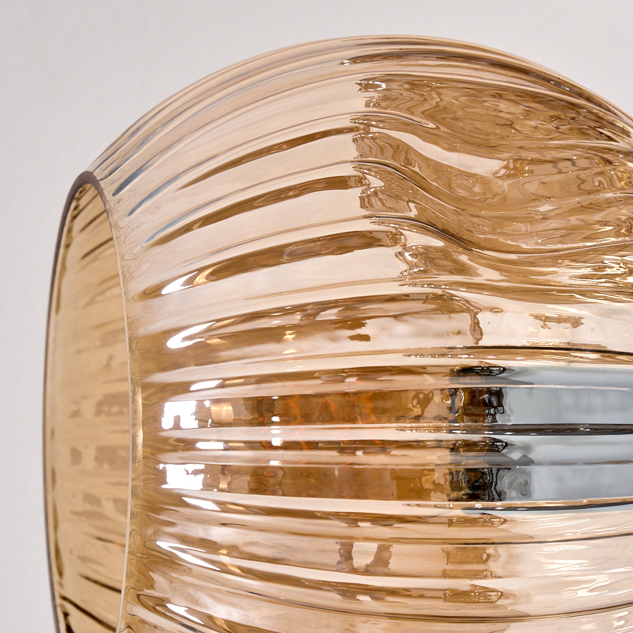 Nahaufnahme eines klaren Glasobjekts mit horizontalen Rillen, die Licht reflektieren. Das Glas ist bernsteinfarben vor weißem Hintergrund.