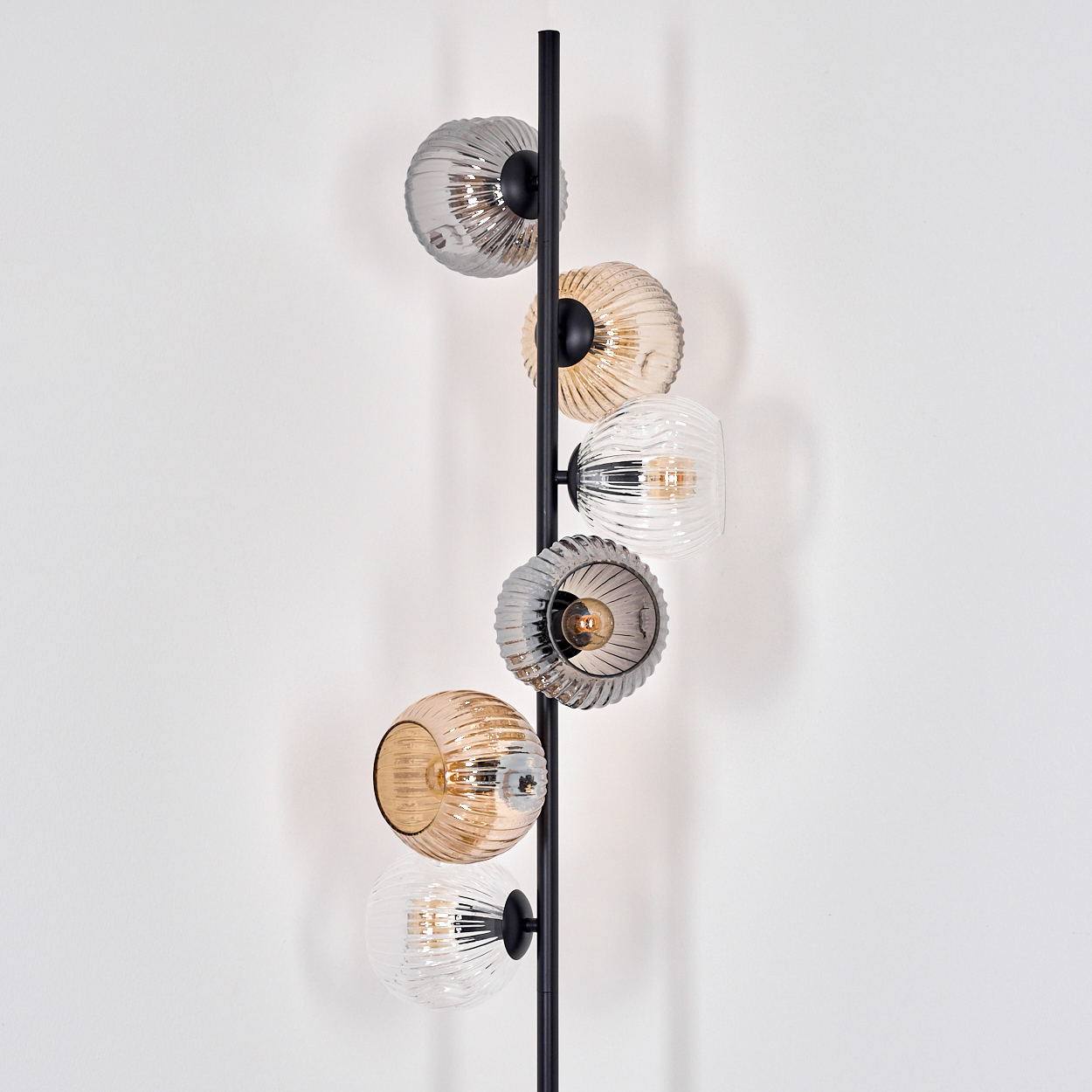 Eine moderne Lampe mit sechs Glaskugeln in verschiedenen Farben. Die Kugeln sind an einer schwarzen Stange an einer weißen Wand befestigt.