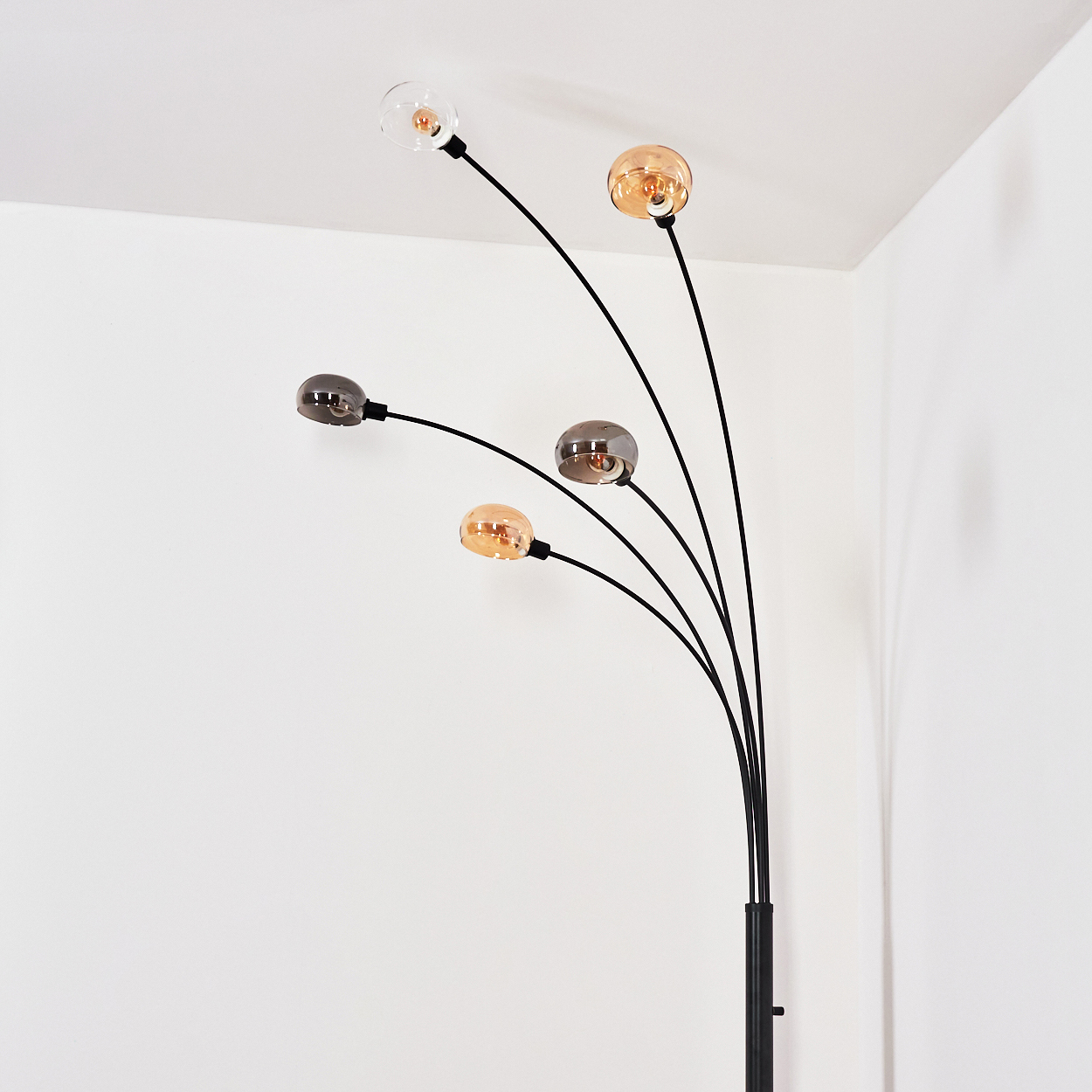 Eine moderne Stehlampe mit fünf Glühbirnen. Die Lichter haben verschiedene Farben: klar, bernsteinfarben und grau. Der Hintergrund sind weiße Wände.