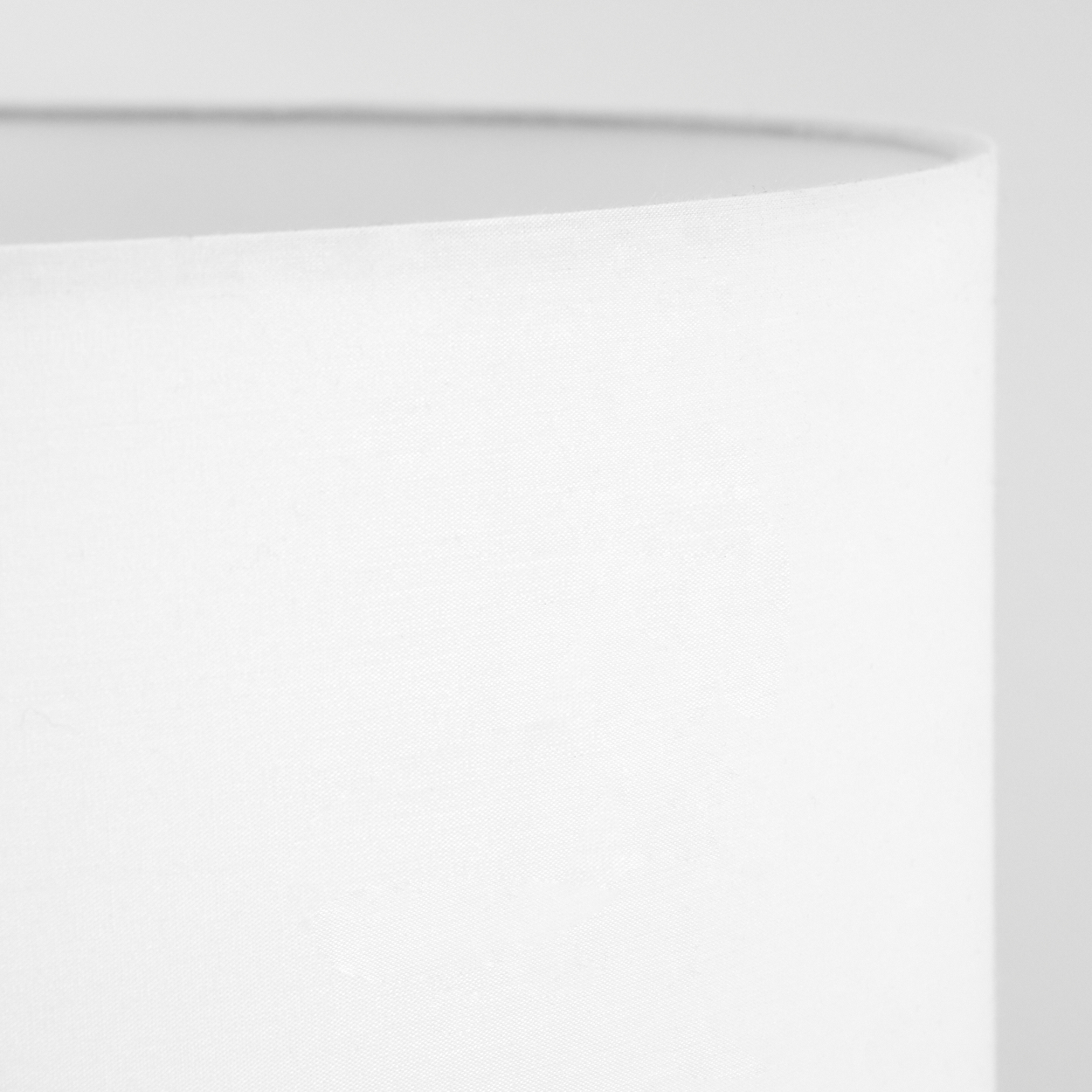 Nahaufnahme eines weißen Lampenschirms. Der Stoff ist strukturiert. Der Hintergrund ist eine weiße Wand, die Oberseite des Schirms ist sichtbar.
