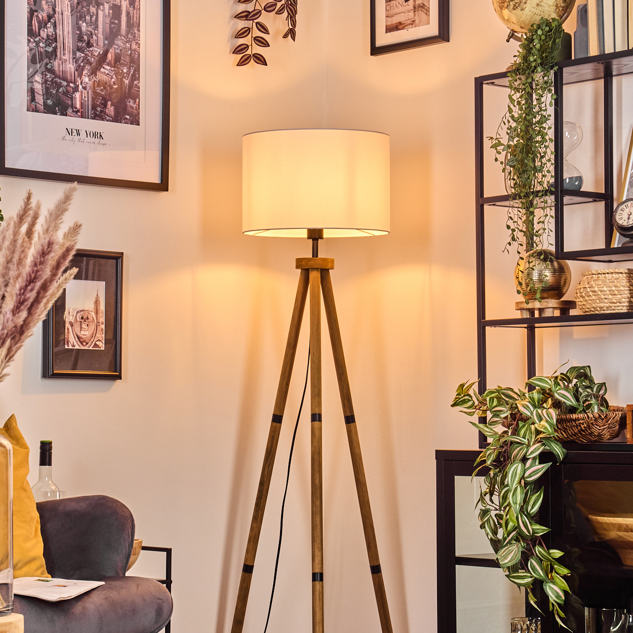 Eine beleuchtete Stativlampe steht im Mittelpunkt. Ein gerahmtes New York-Bild und ein Regal mit Pflanzen befinden sich links bzw. rechts.