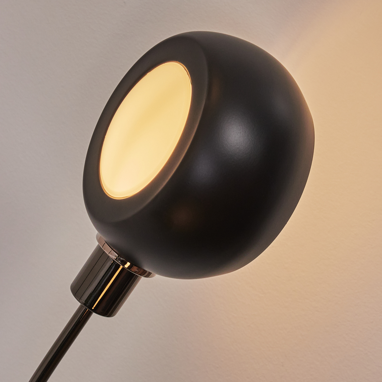 Nahaufnahme einer schwarzen Lampe mit rundem Kopf und hellem, warmem Licht. Der Hintergrund ist ein Gradient aus Weiß und Gelb.