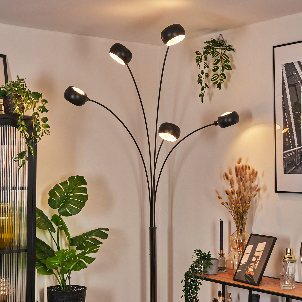 Eine moderne schwarze Stehlampe mit fünf Lichtern. Pflanzen und Dekorationen füllen die Ecken eines Raumes.