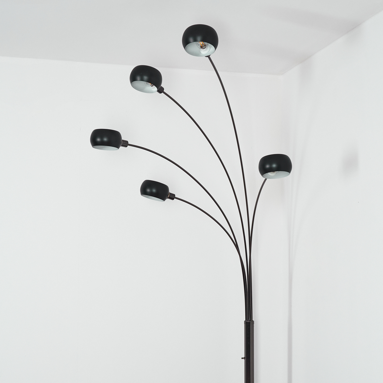 Eine schwarze Stehlampe mit fünf Lichtern. Die Lampen zeigen in verschiedene Richtungen. Der Hintergrund ist eine weiße Wand.