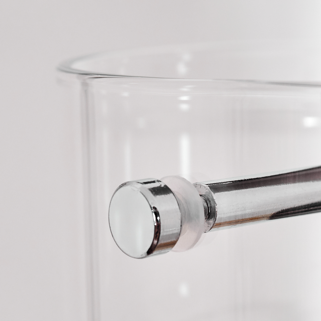 Nahaufnahme eines klaren Glases mit einem verchromten Metallgriff. Der Hintergrund ist eine weiße Oberfläche.