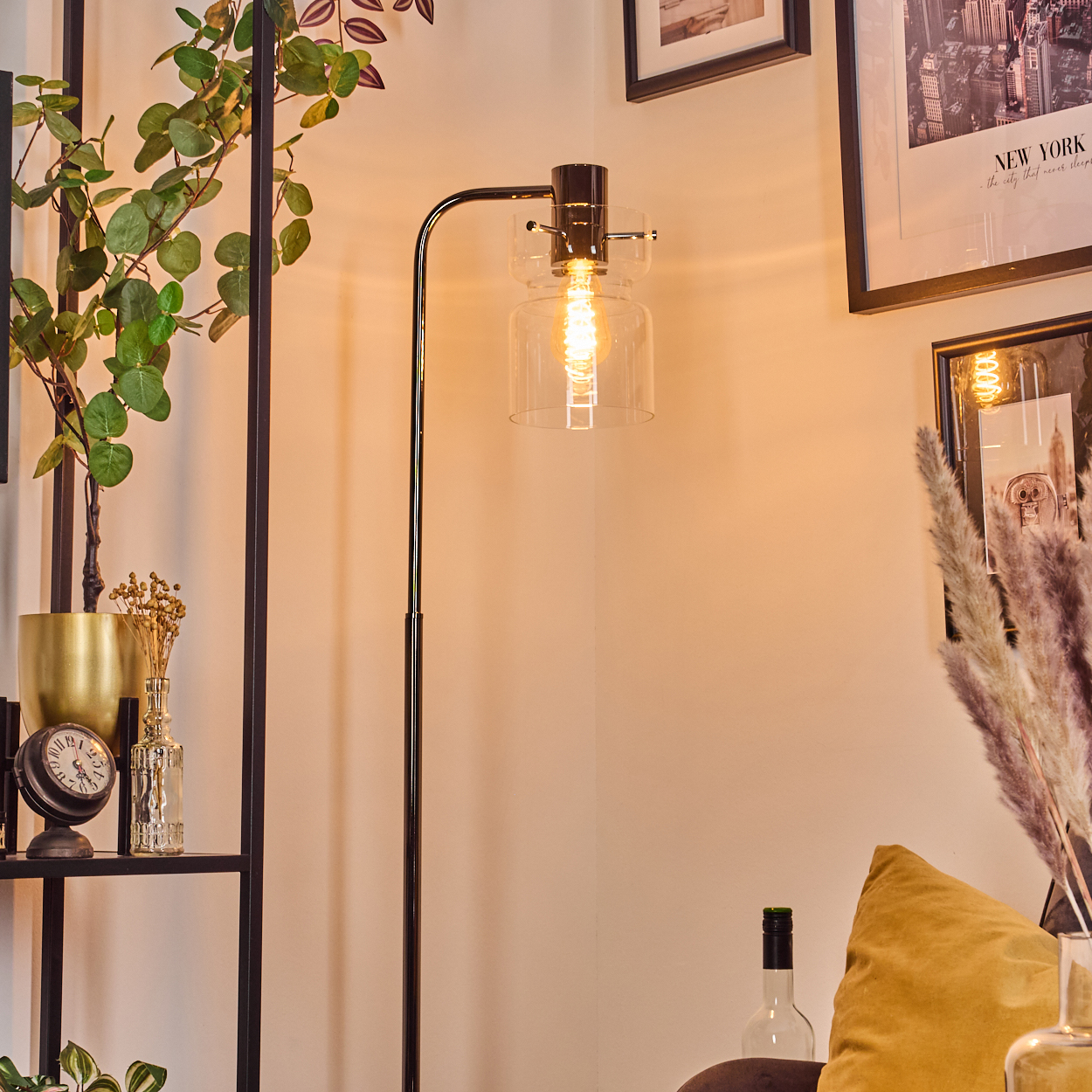 Eine moderne Stehlampe mit Glasschirm beleuchtet eine Ecke mit Pflanzen, einem Regal und gerahmten Bildern.