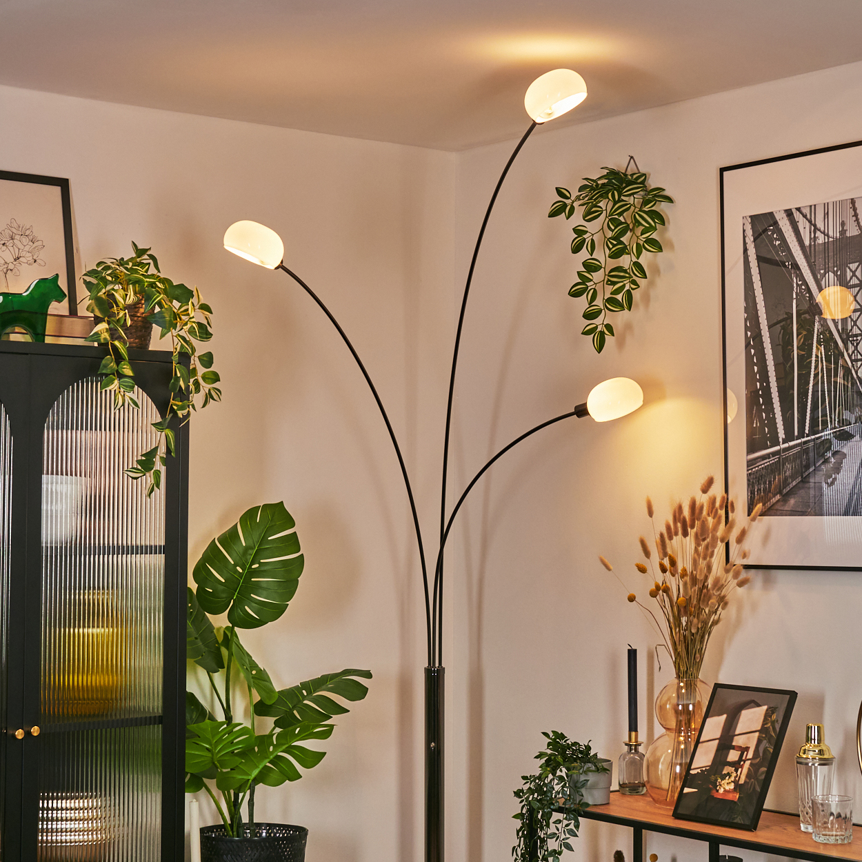 Ein modernes Wohnzimmer mit schwarzer Lampe, Pflanzen, Brückenbild und schwarzem Schrank.
