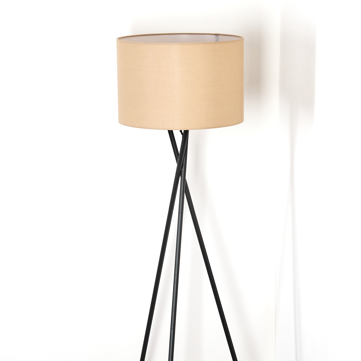 Ein beigefarbener Lampenschirm sitzt auf einer schwarzen Stativ-Stehlampe. Der Hintergrund ist eine weiße Wand mit Schatten.
