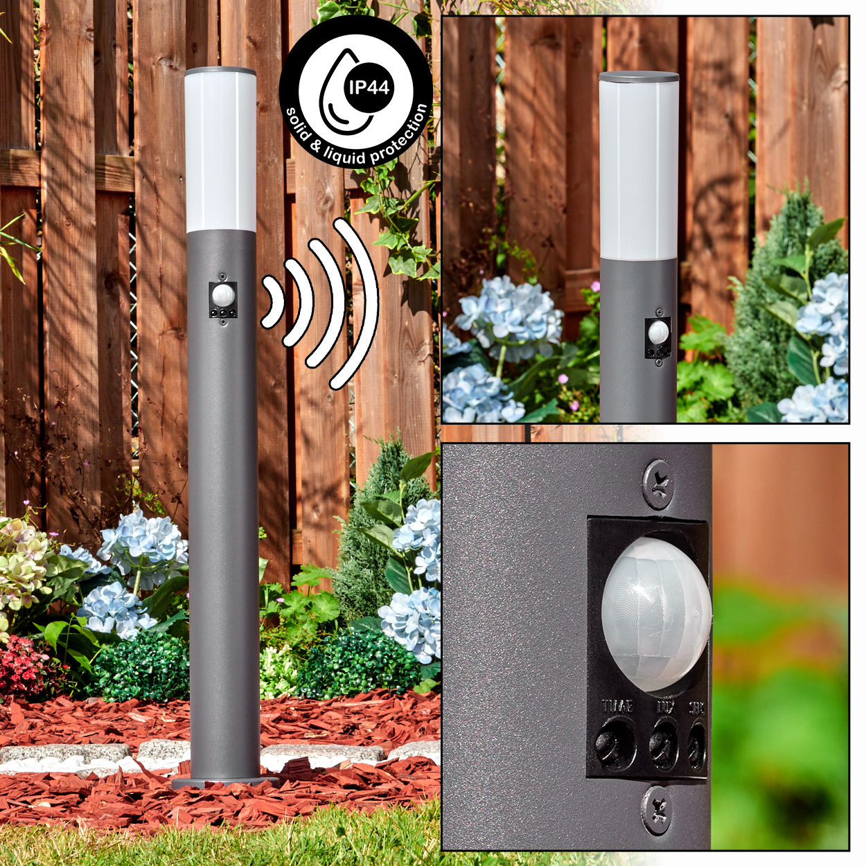 Eine graue Außenleuchte mit weißem Oberteil, Sensor und Schutzsymbol. Sie befindet sich in einem Garten mit Blumen und einem Holzzaun im Hintergrund.