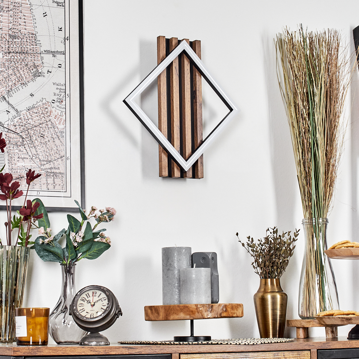 Weiß gerahmtes Kunstwerk mit Holzhintergrund. Eine Karte, eine Vase mit Blumen, eine Uhr, Kerzen und eine Vase mit getrockneten Pflanzen befinden sich auf einem Regal.