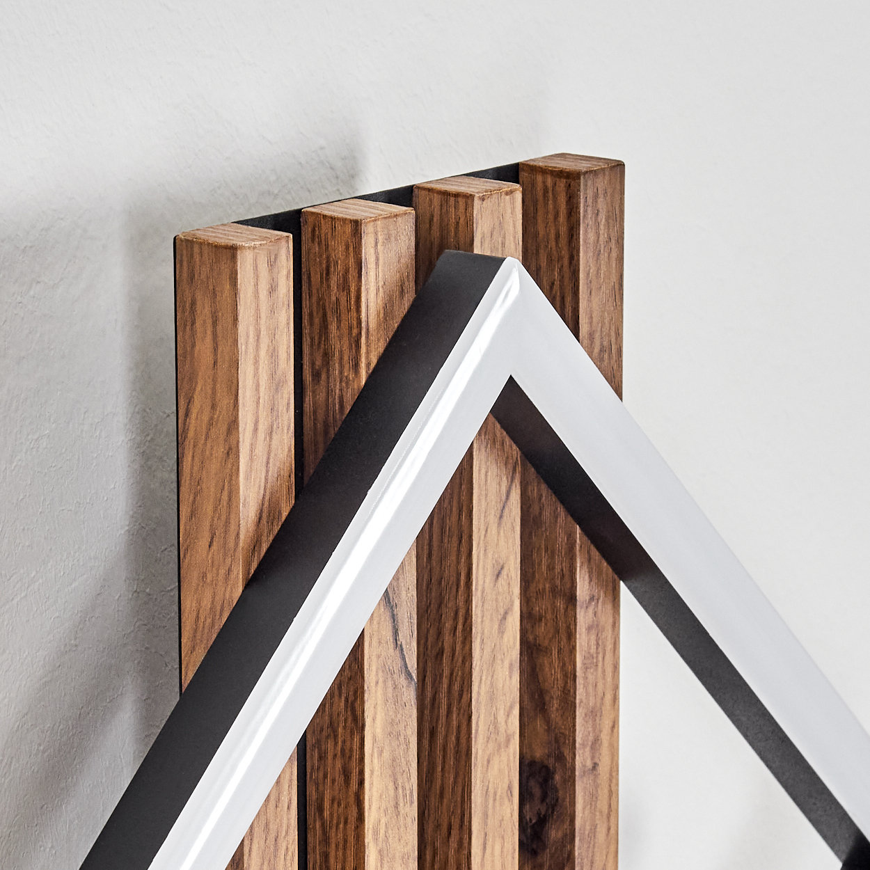 Holzpaneel mit vertikalen Planken. Ein schwarz-weißer geometrischer Rahmen ist auf dem Paneel platziert. Weiße Wand im Hintergrund.