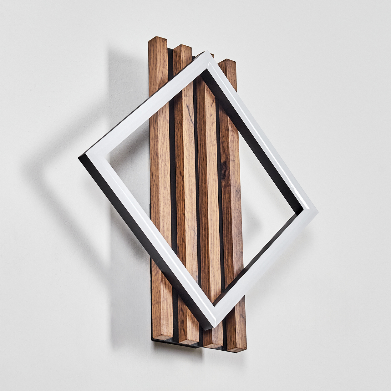 Moderne Wanddekoration. Sie zeigt eine Holzlattenwand mit einem weißen quadratischen Rahmen, der auf einer weißen Wand montiert ist.