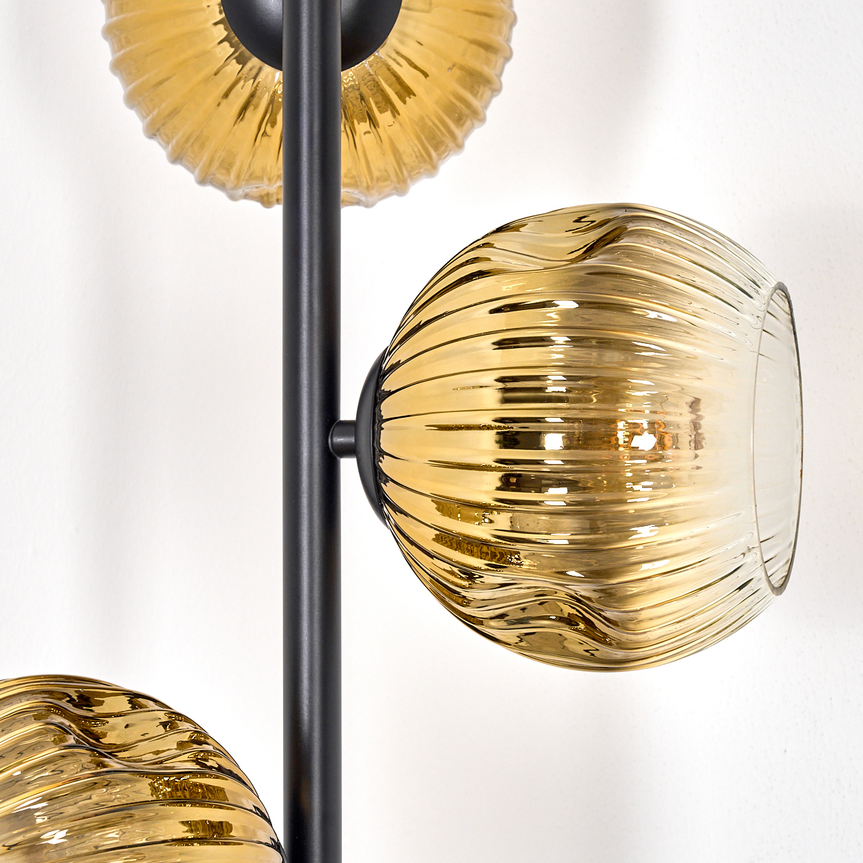 Nahaufnahme einer modernen Lampe mit drei goldenen Glasschirmen. Schwarze Metallstruktur vor weißer Wand.