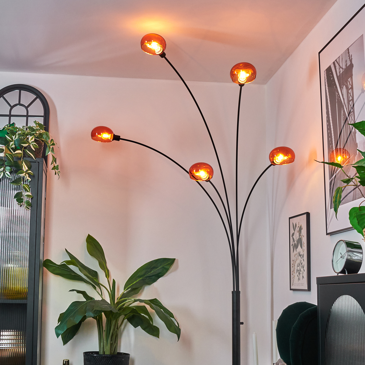 Ein modernes Wohnzimmer mit einer schwarzen Lampe mit orangefarbenen Lichtern. Es gibt Pflanzen, einen Schrank und ein gerahmtes Bild.
